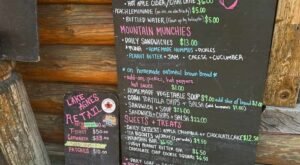 Chalkboard menu outside the rustic Lake Agnes Tea House lists hot drinks, snacks, sandwiches, soups, sweets, and retail items with prices in colorful handwriting for hikers on the Lake Agnes Tea House Trail.