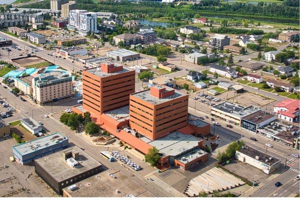 Aerial view of a cityscape in Alberta featuring two adjacent mid-rise red brick office buildings, surrounded by streets, parking lots, and smaller commercial structures—one of the top destinations for urban exploration.