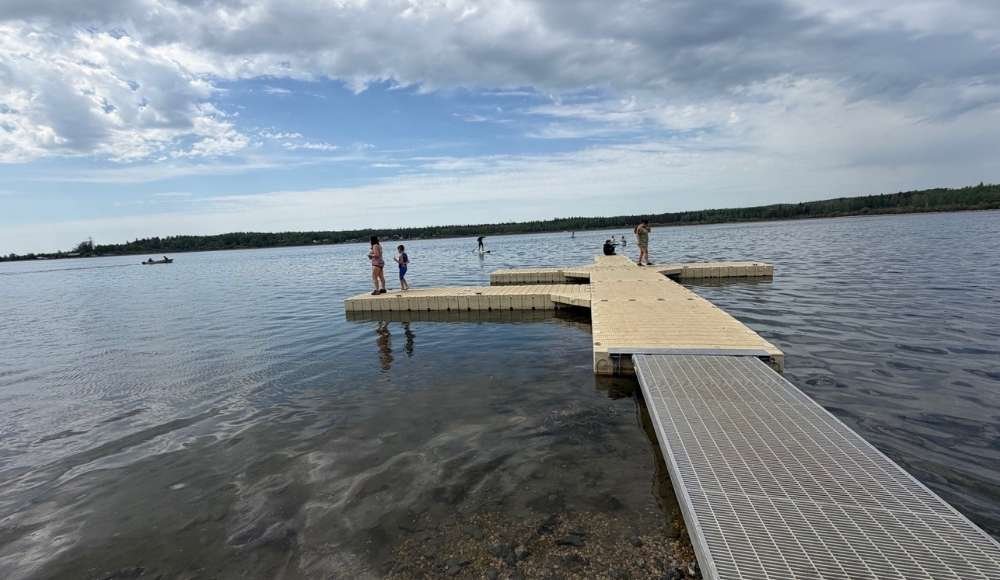 A floating dock extends into Wabamun Lake at Wabamun Lake Provincial Park, with several people standing and walking on it under a partly cloudy sky—one of the scenic lakes near Edmonton perfect for swimming and relaxing.