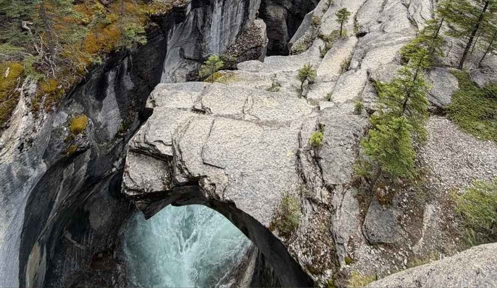 A natural rock bridge spans over a rushing river at Mistaya Canyon Banff