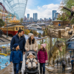 A family walks in front of a collage showing a train, cityscape, zoo animals, an indoor pool, a dinosaur exhibit, and a rock climbing wall.
