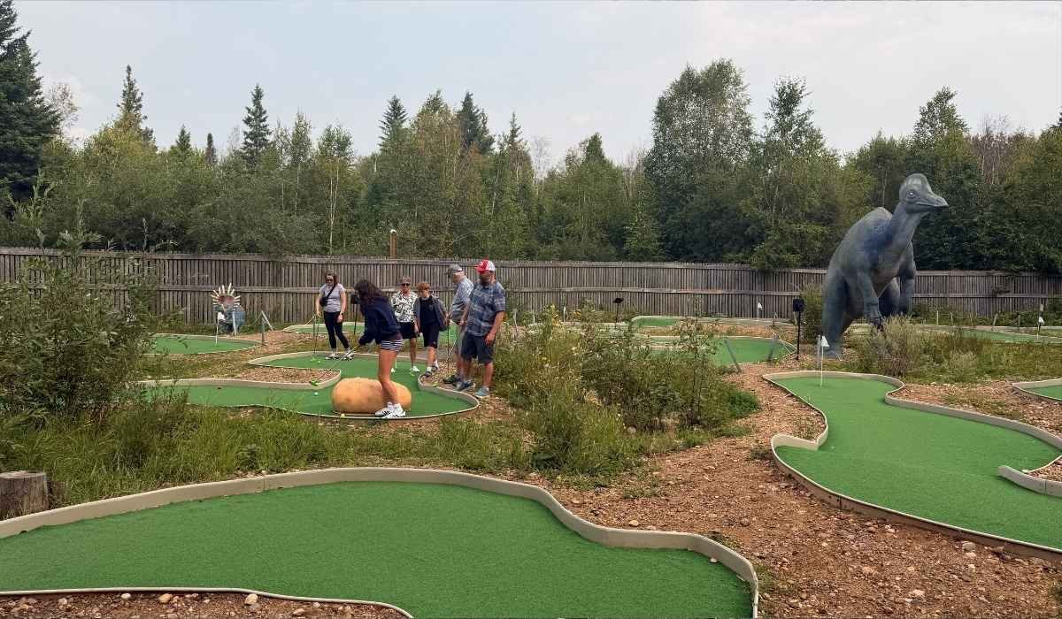 People play mini-golf surrounded by artificial dinosaur sculptures at the Jurassic Forest 18-hole dinosaur mini golf course called Journey to Extinction